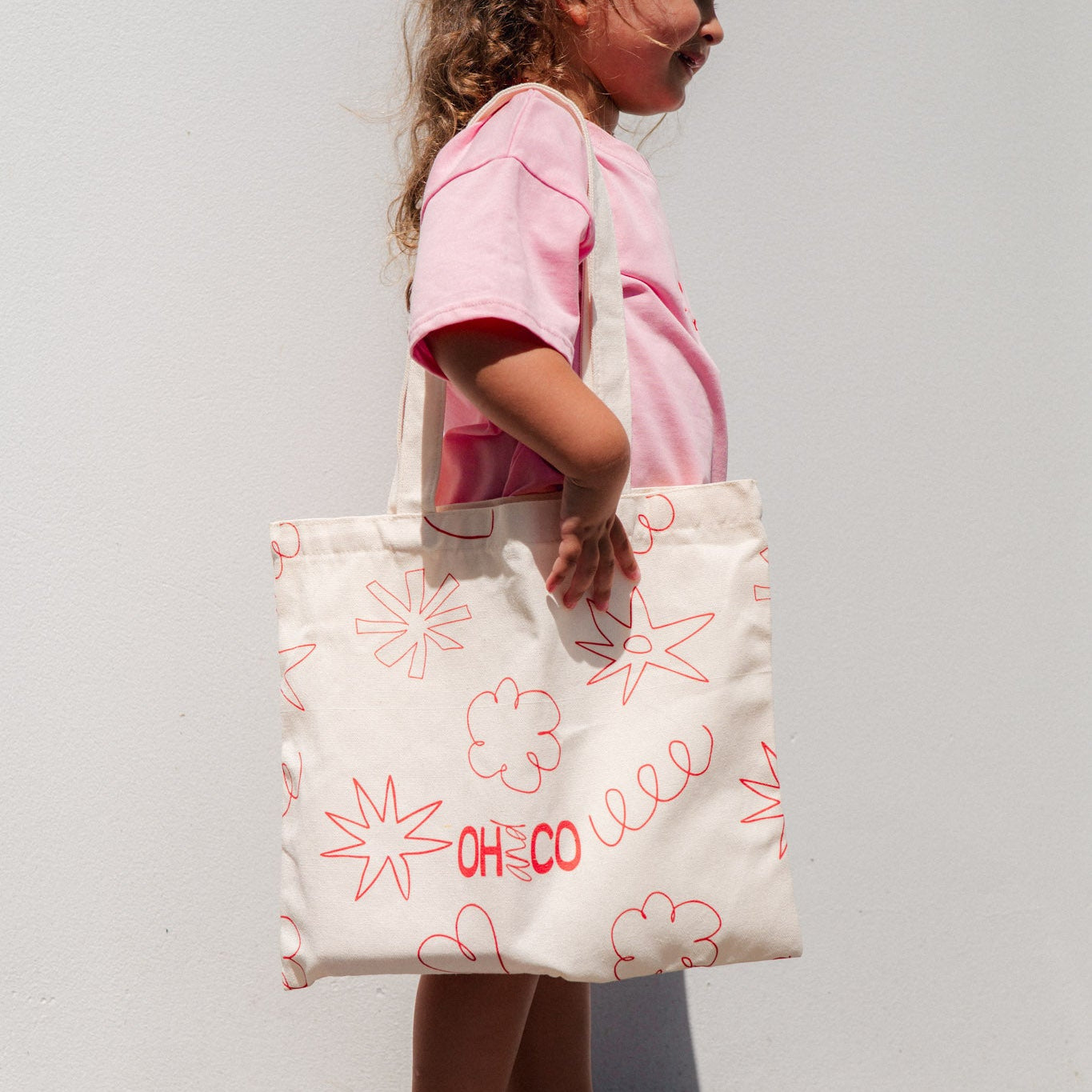 Child holding a white tote bag with red designs and text against a plain background
