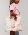 Child holding a white tote bag with red designs and text against a plain background