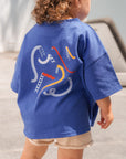 Child wearing a blue t-shirt with colorful graphic design outdoors