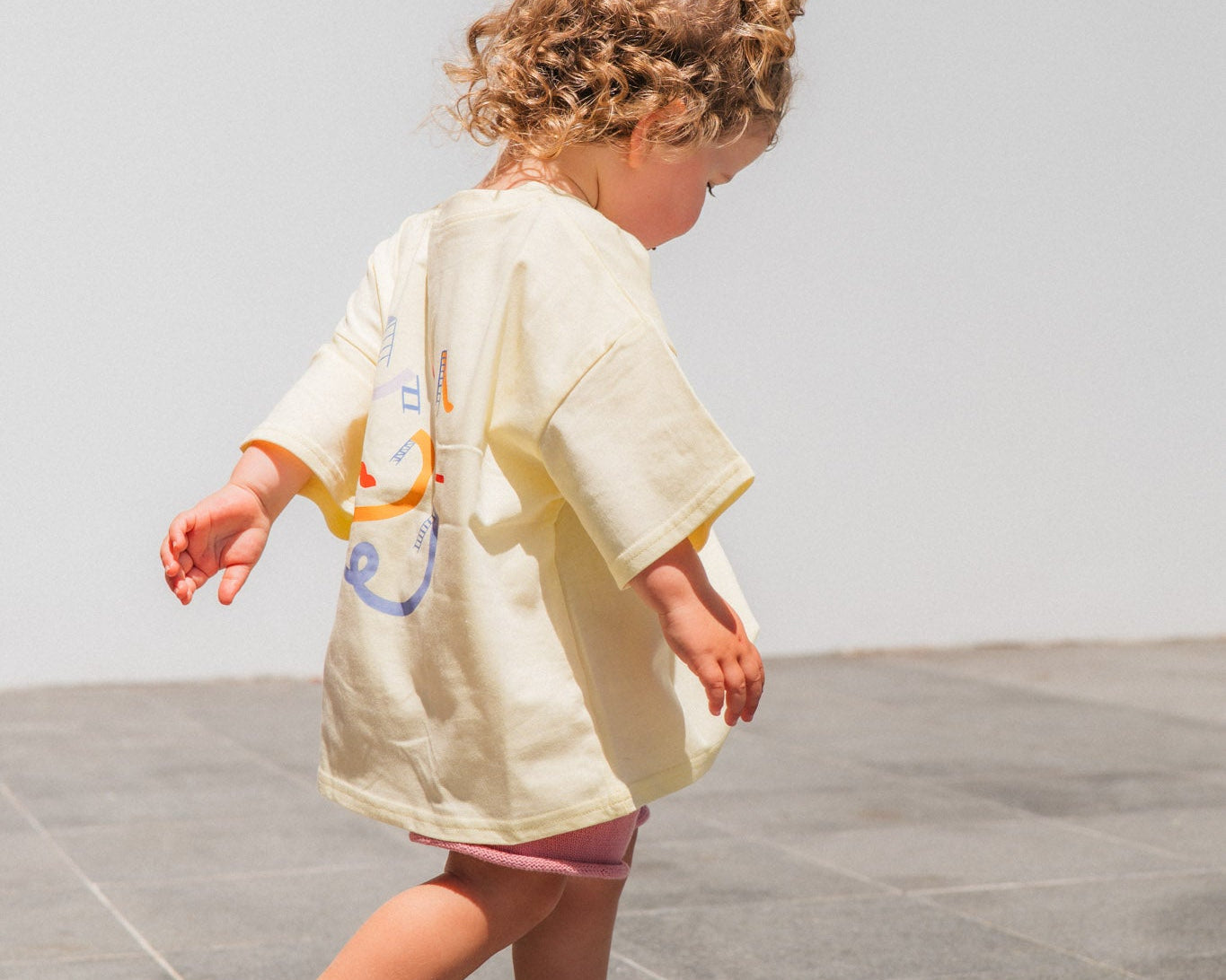 Child walking on a tiled floor wearing a light-colored outfit with colorful designs.