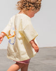 Child walking on a tiled floor wearing a light-colored outfit with colorful designs.