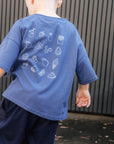 Child wearing a blue t-shirt with white graphics and dark pants, standing on a pavement.