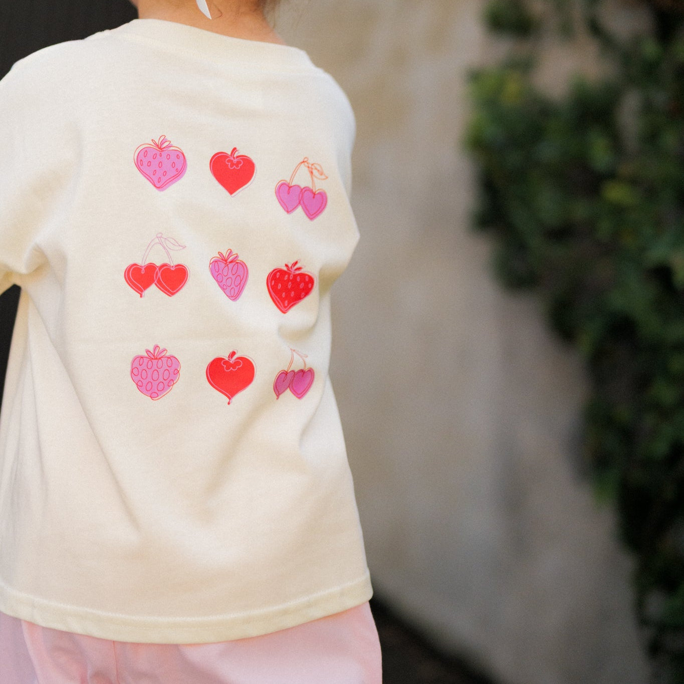 Child wearing a berry boujee tee with red and pink heart designs outdoors.