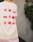 Child wearing a berry boujee tee with red and pink heart designs outdoors.