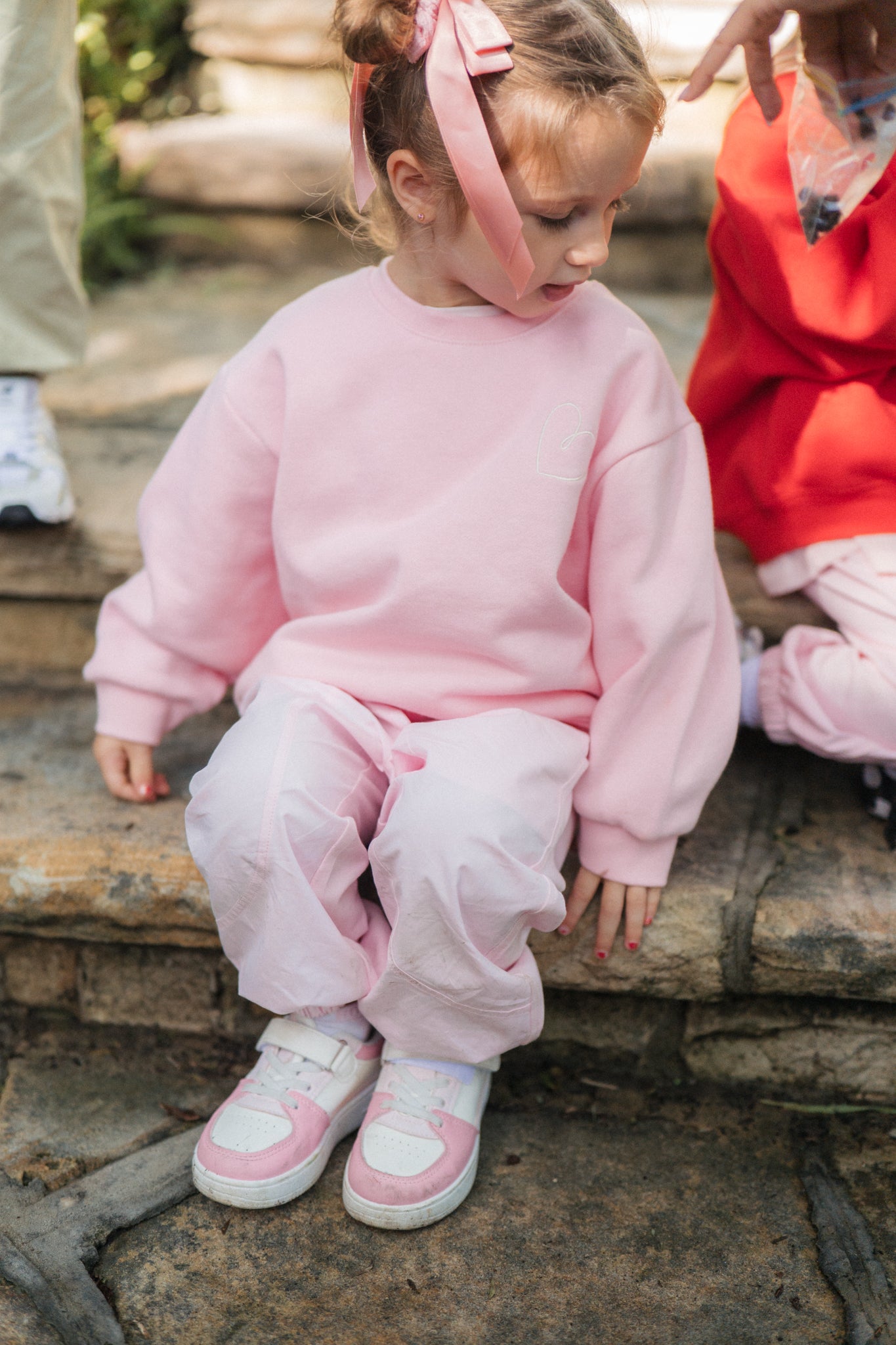 Child wearing a pink outfit sitting on stone steps.
