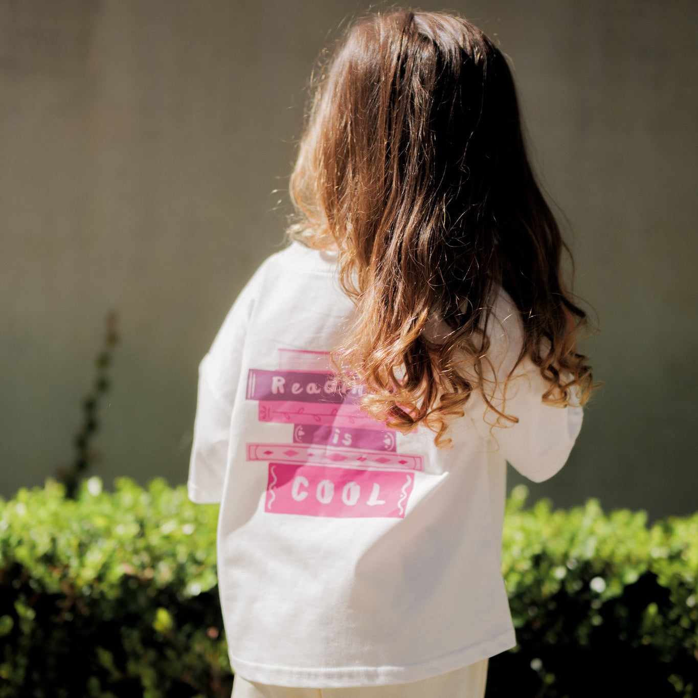 Person wearing a white shirt with text, standing outdoors with greenery in the background