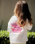 Person wearing a white shirt with text, standing outdoors with greenery in the background