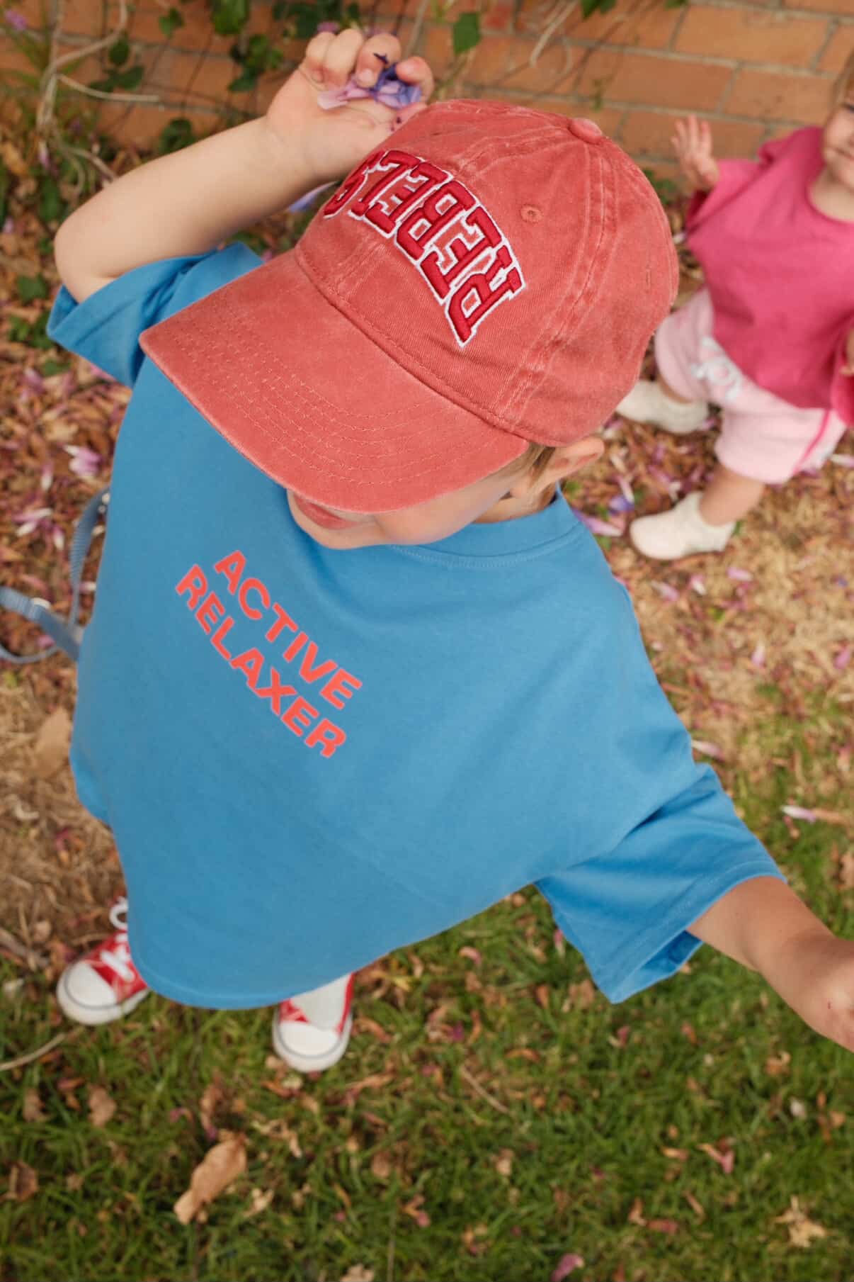 Child wearing blue ACTIVE RELAXER TEE with text, standing outdoors on grass.
