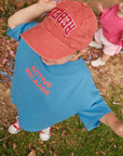 Child wearing blue ACTIVE RELAXER TEE with text, standing outdoors on grass.