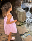 Young girl in a pink dress standing near a small waterfall