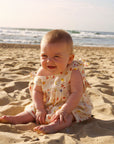 Baby sitting on a sandy beach with ocean in the background