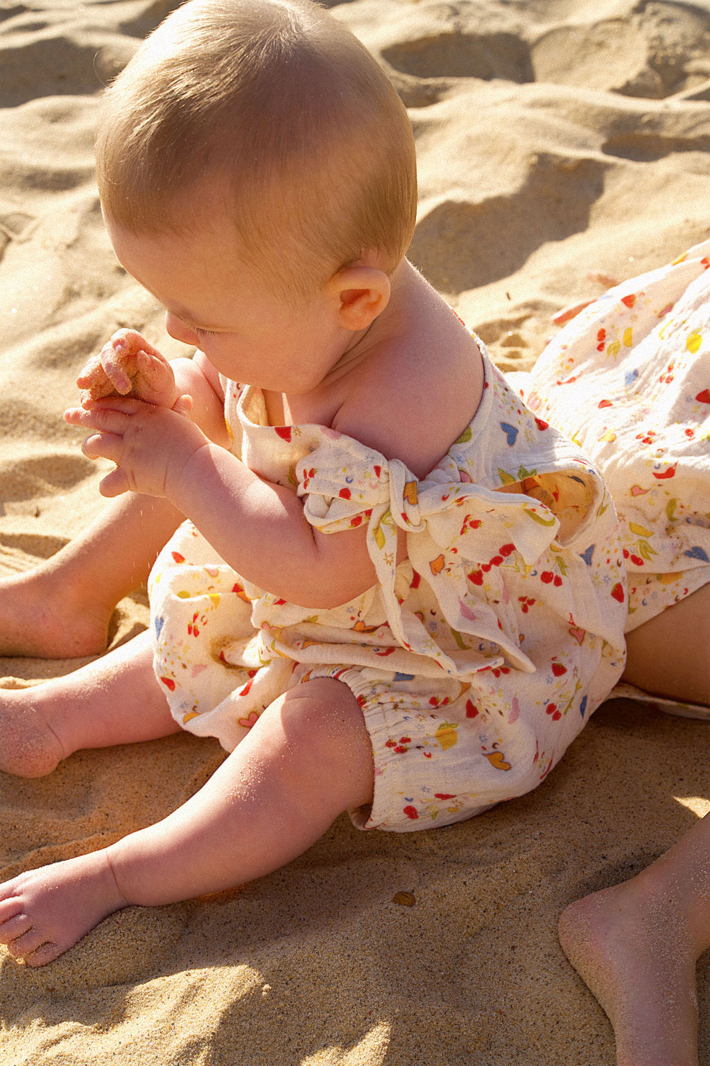 Baby in a floral romper sitting on sand