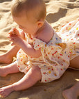 Baby in a floral romper sitting on sand