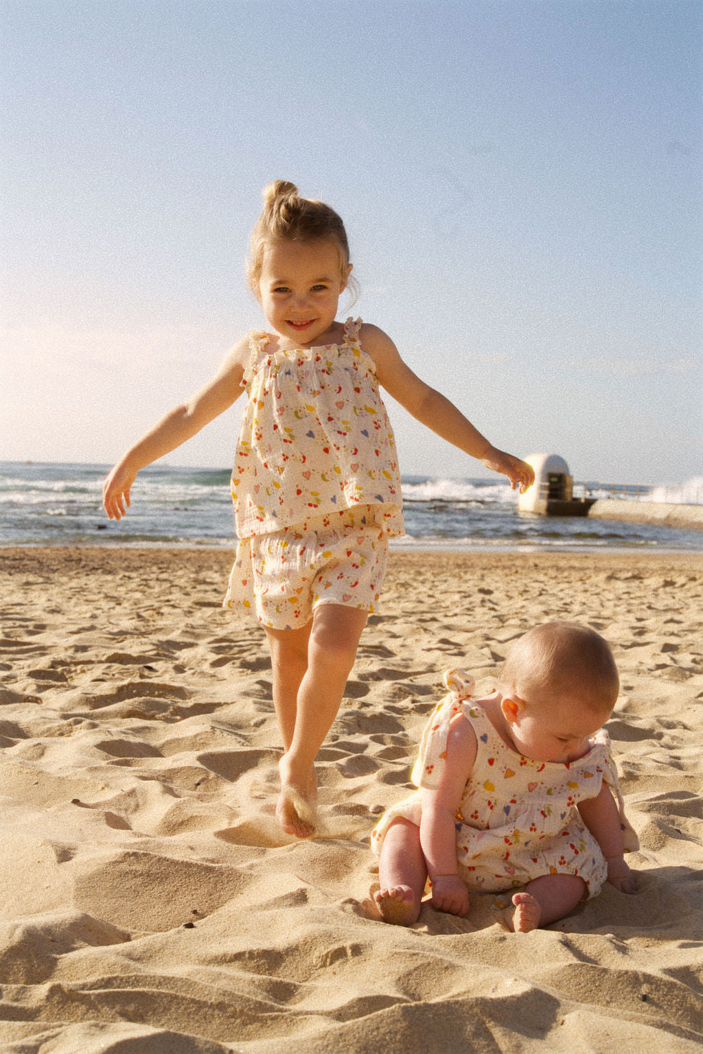 Two children in matching dresses playing on a sandy beach.