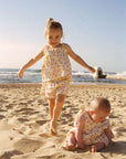 Two children in matching dresses playing on a sandy beach.