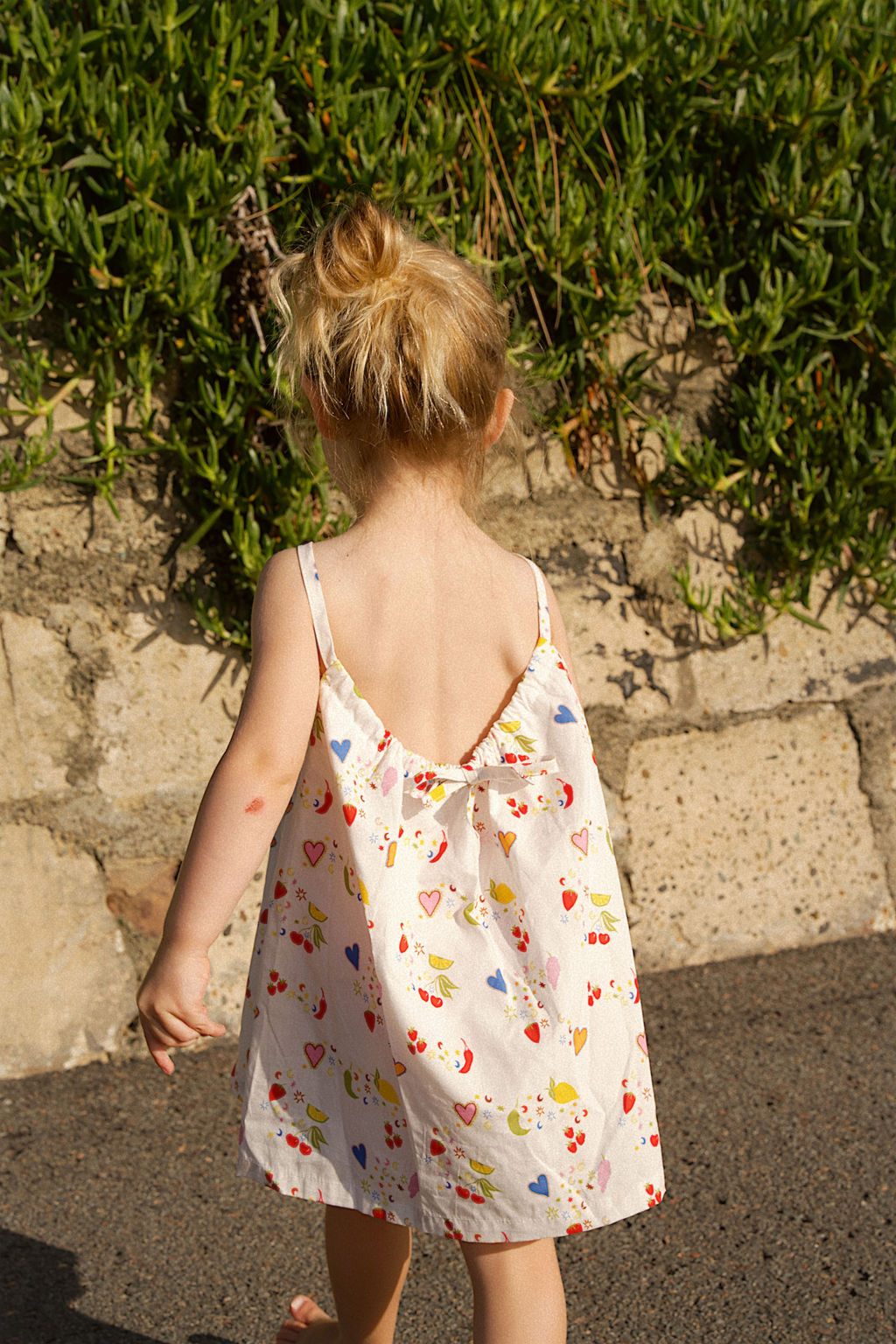 Child in a floral dress walking on a sidewalk with greenery in the background