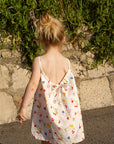 Child in a floral dress walking on a sidewalk with greenery in the background
