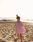 Child in a pink dress standing on a sandy beach with the ocean in the background