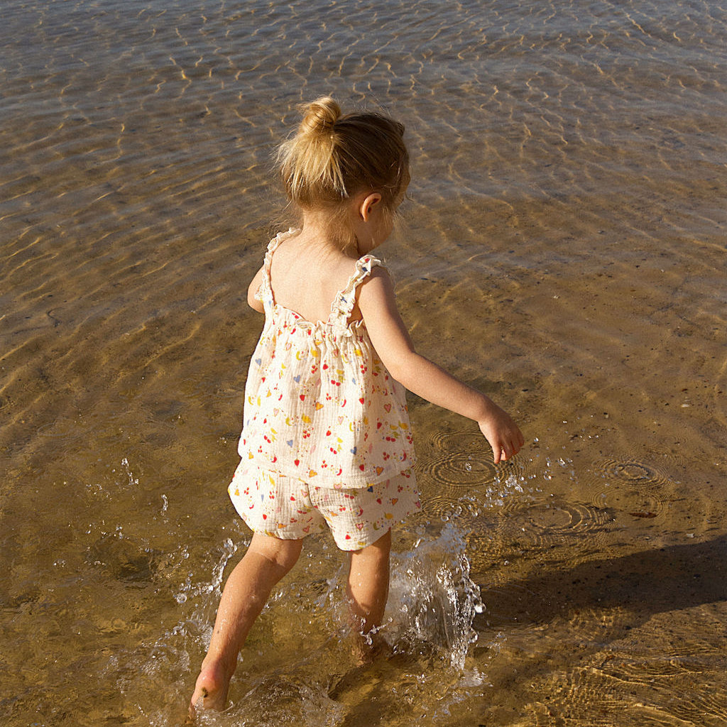 Child in a floral matching set walking in shallow water at the beach