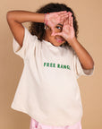 A child wearing a cream-colored oversized t-shirt with green 'FREE RANGE.' text on the chest, paired with light pink pants, posing against a solid beige background.