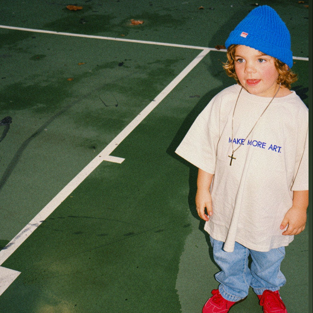 Child wearing a blue beanie and grey tee shirt on a tennis court