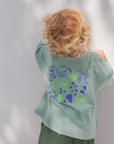 Child wearing a green snack lover tee with blue designs against a white wall