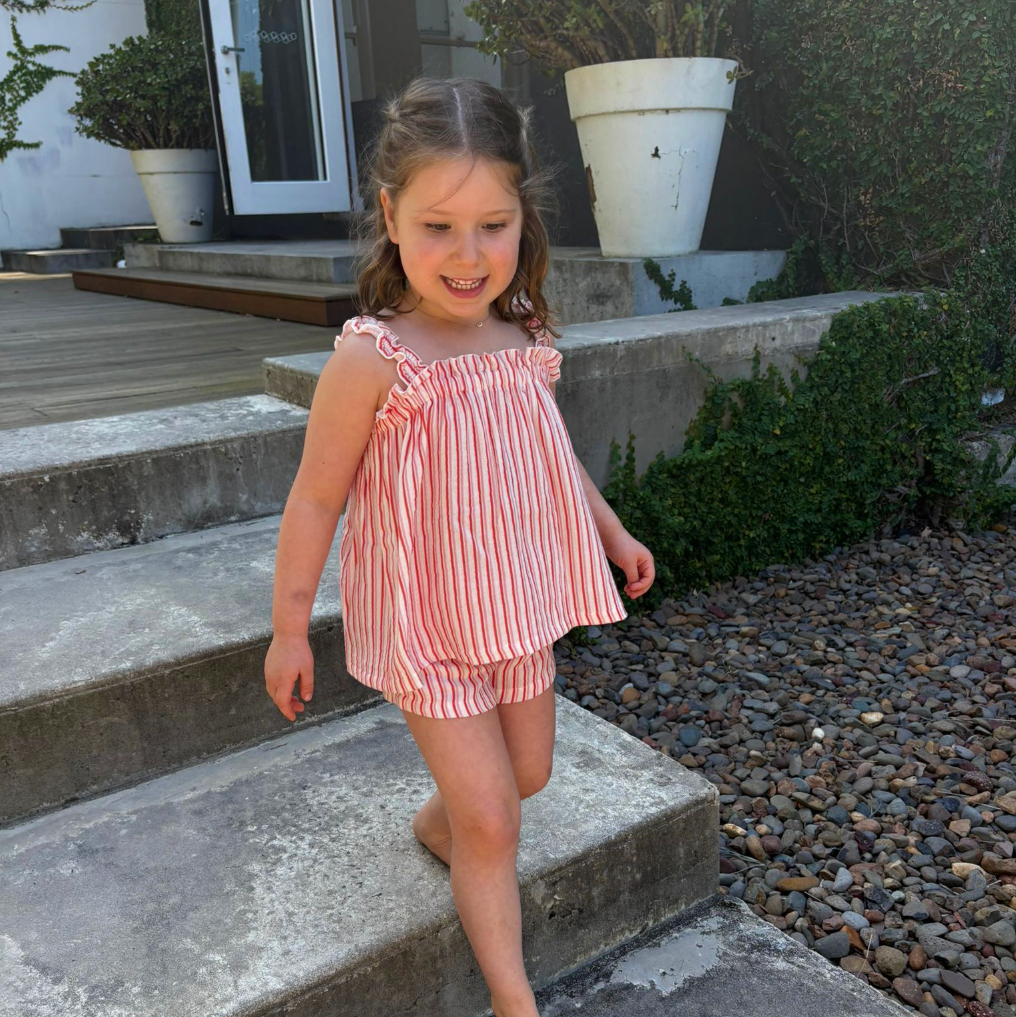 Young girl in a pink striped outfit standing on outdoor steps.