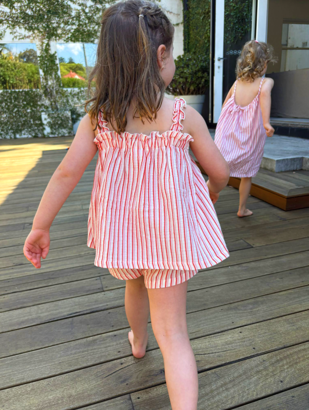 Two young girls in matching pink striped dresses walking on a wooden deck.