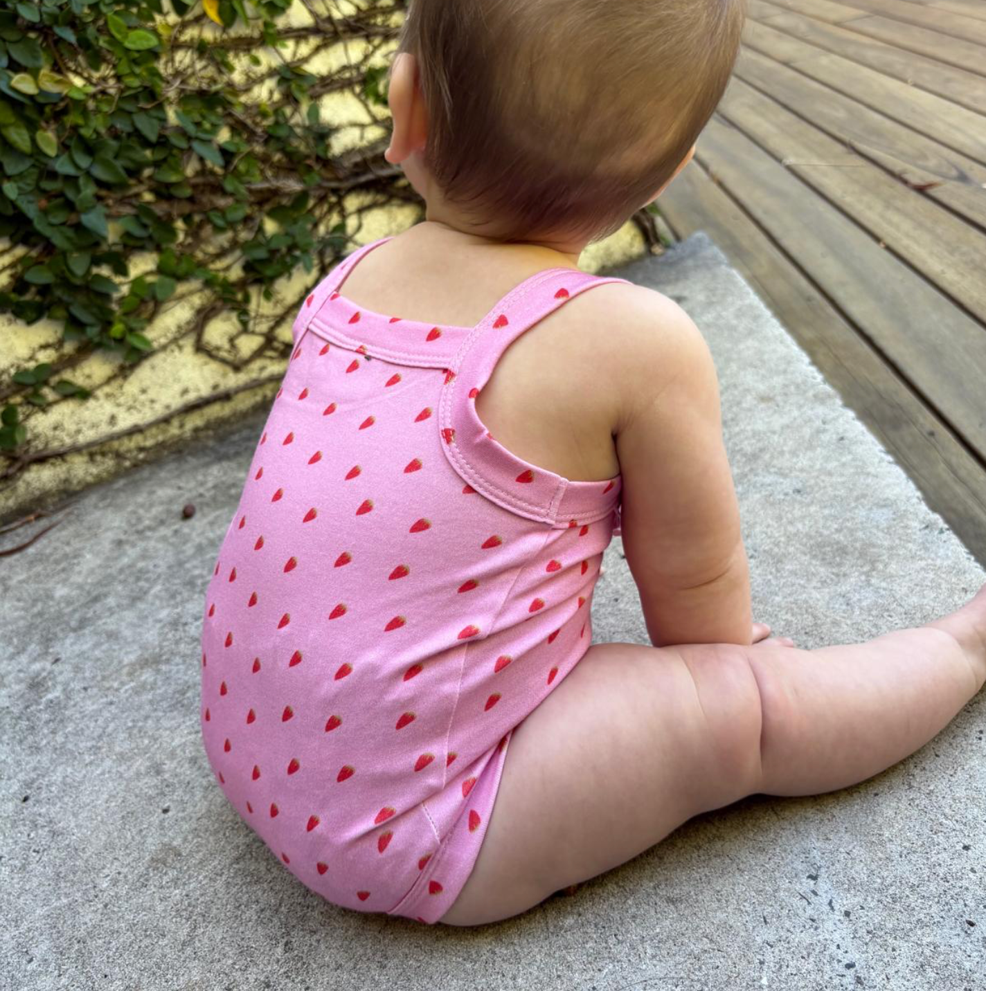 Child wearing a pink outfit with red patterns sitting on a concrete surface.