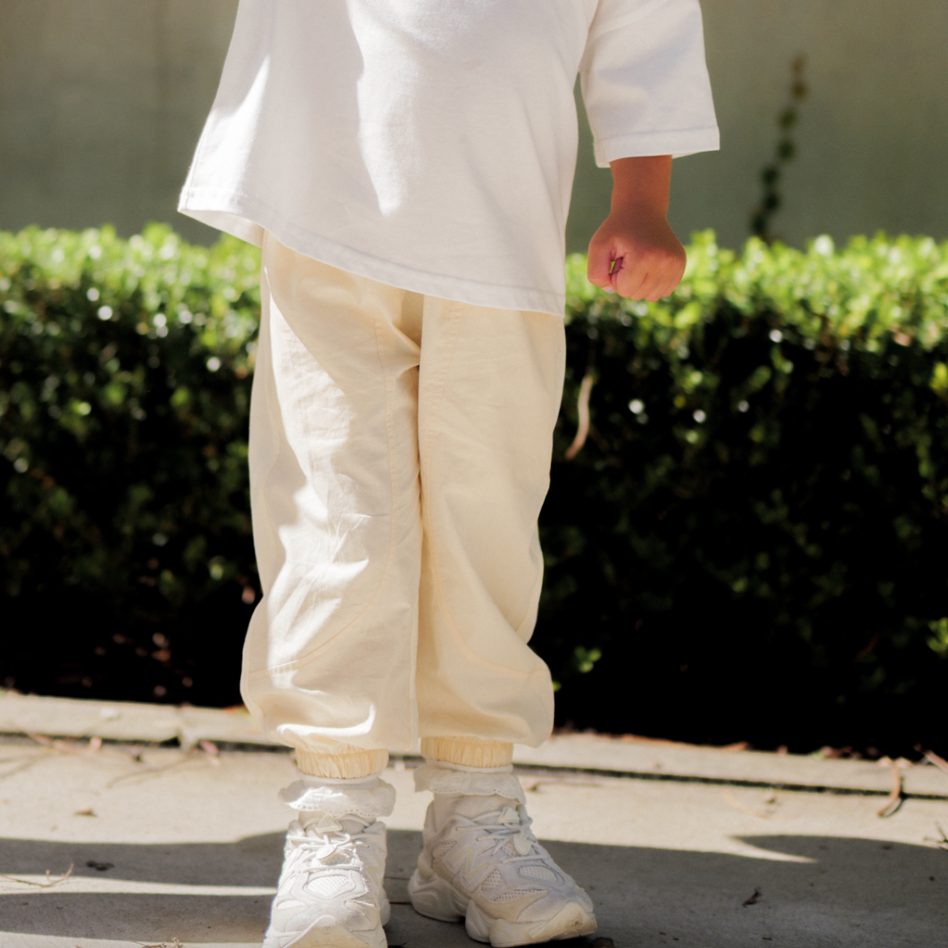 Person wearing beige pants and white shoes standing on a concrete surface with greenery in the background.