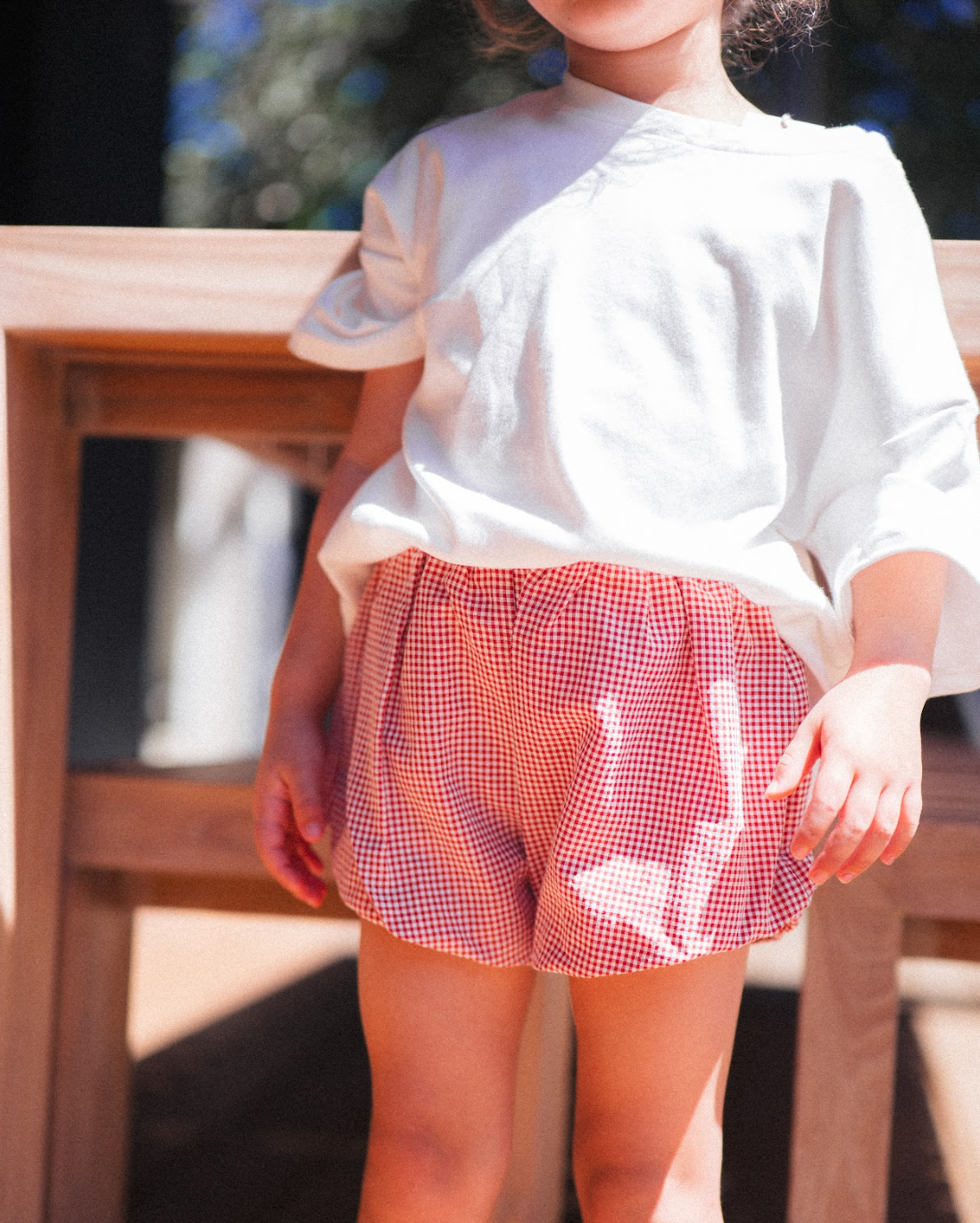 Child wearing a white top and red checkered shorts outdoors