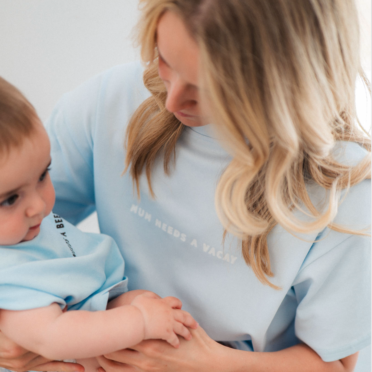 Woman holding a child wearing matching light blue shirts with text.
