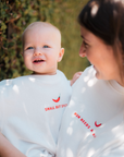 Woman and baby wearing matching white shirts with text in a natural setting
