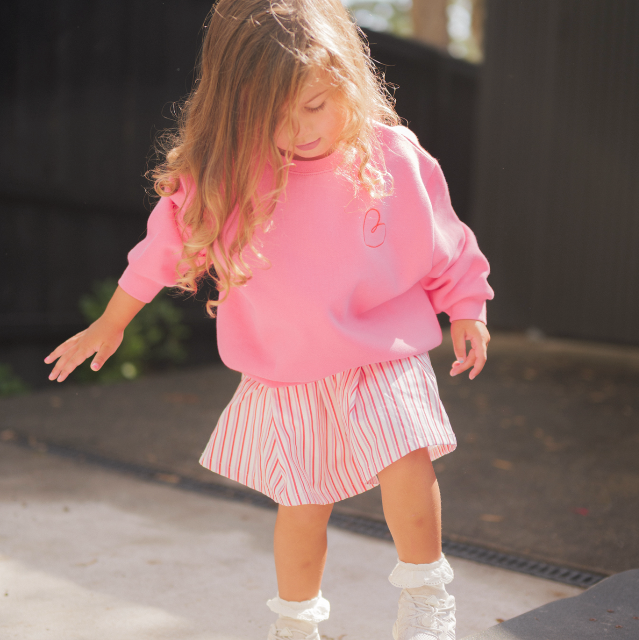 Child in pink sweatshirt and skirt standing on a skateboard