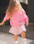 Child in pink sweatshirt and skirt standing on a skateboard