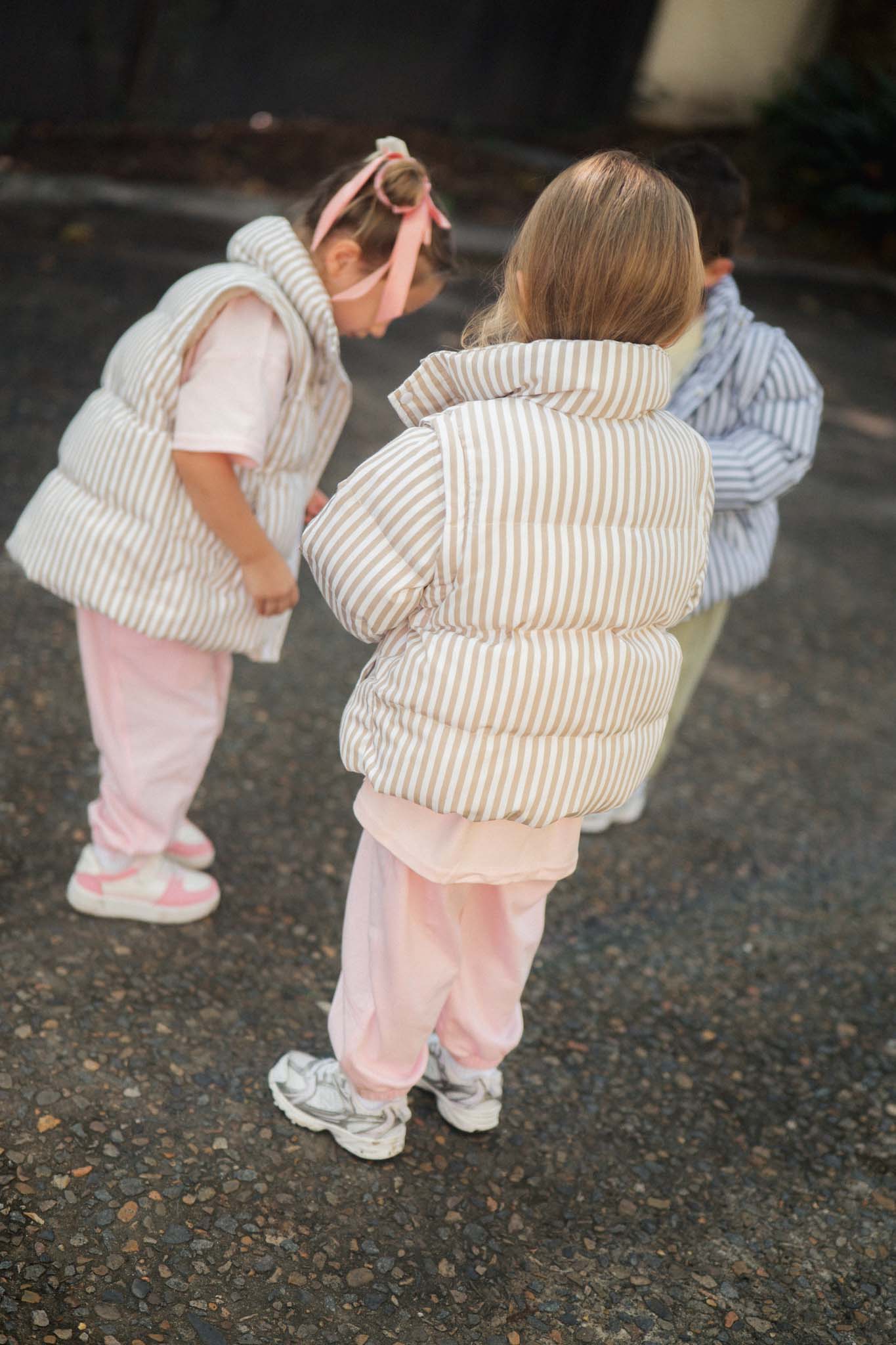 children in striped puffer jackets walking on a street.