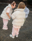 children in striped puffer jackets walking on a street.