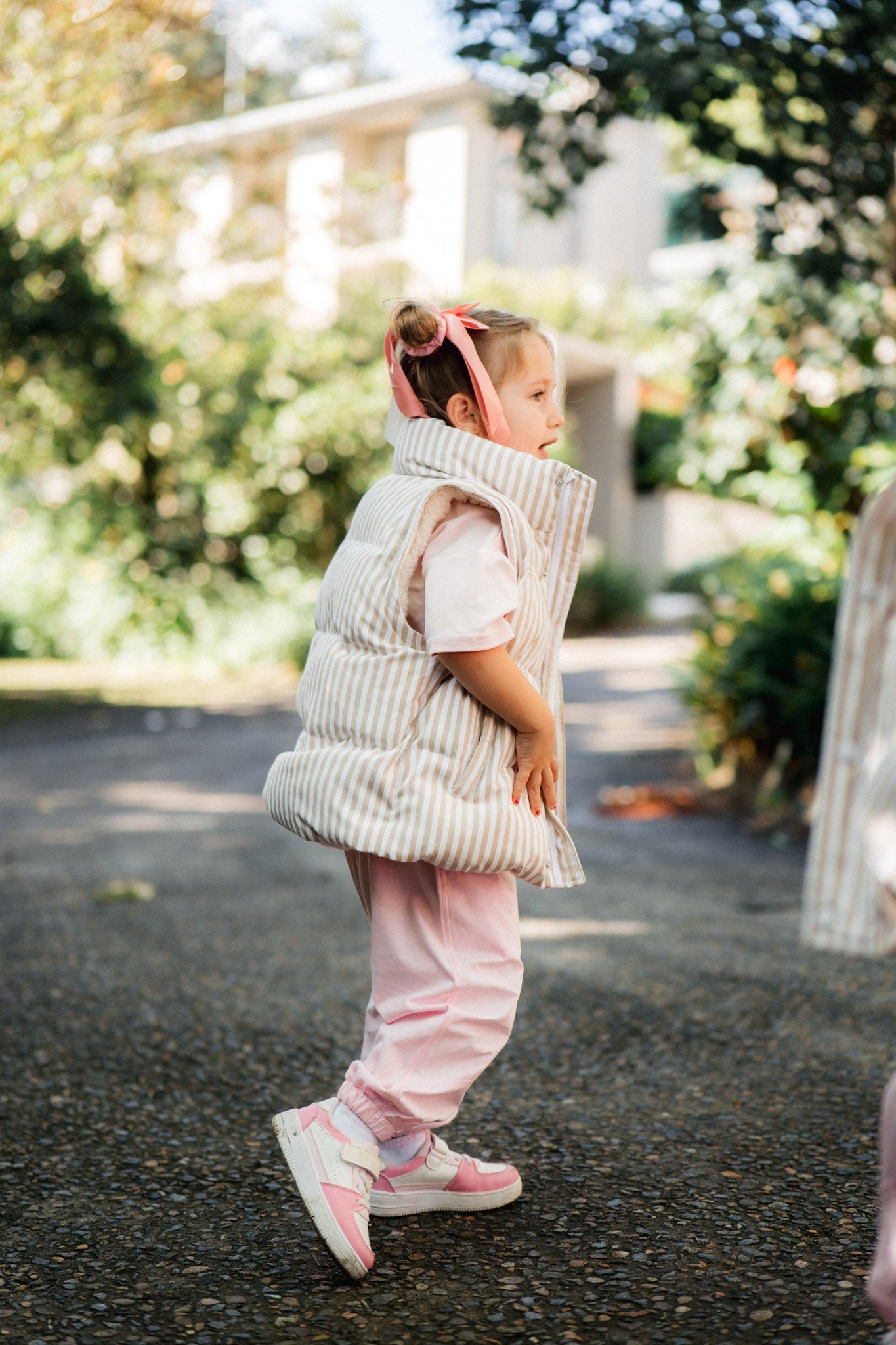 Child in a puffer vest and pink pants walking outdoors with trees in the background