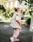 Child in a puffer vest and pink pants walking outdoors with trees in the background
