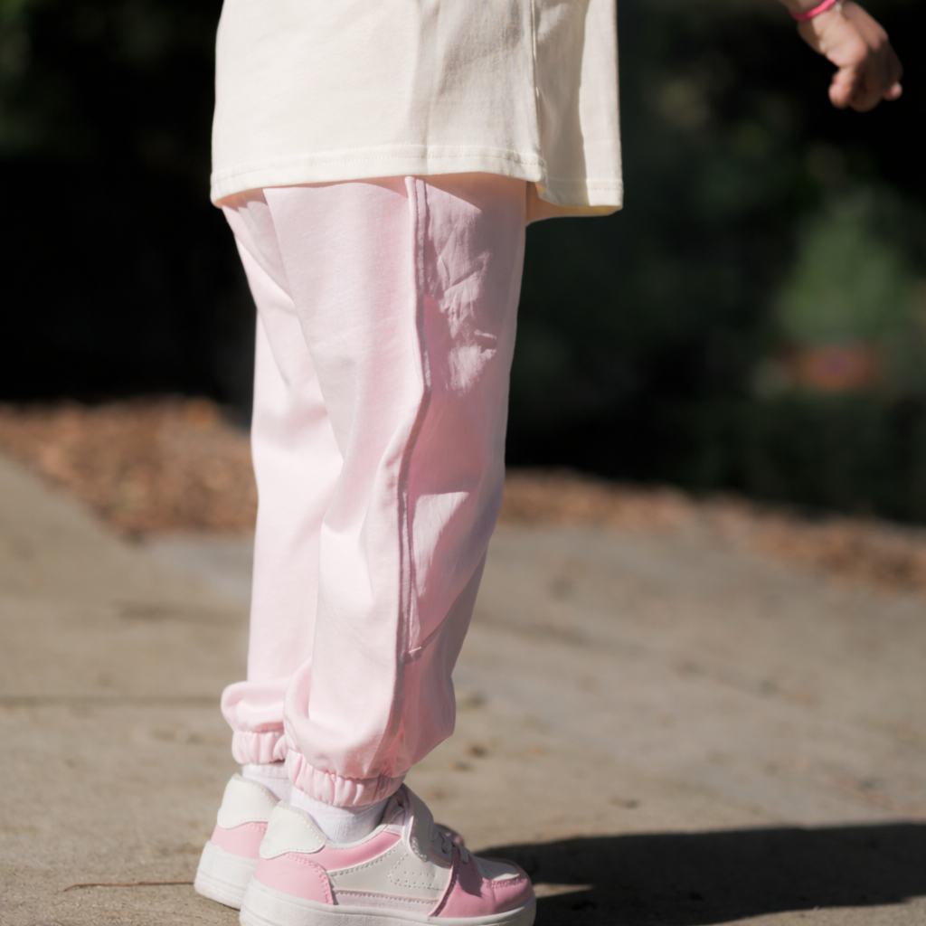 Person wearing light pink pants and white sneakers on a blurred outdoor background