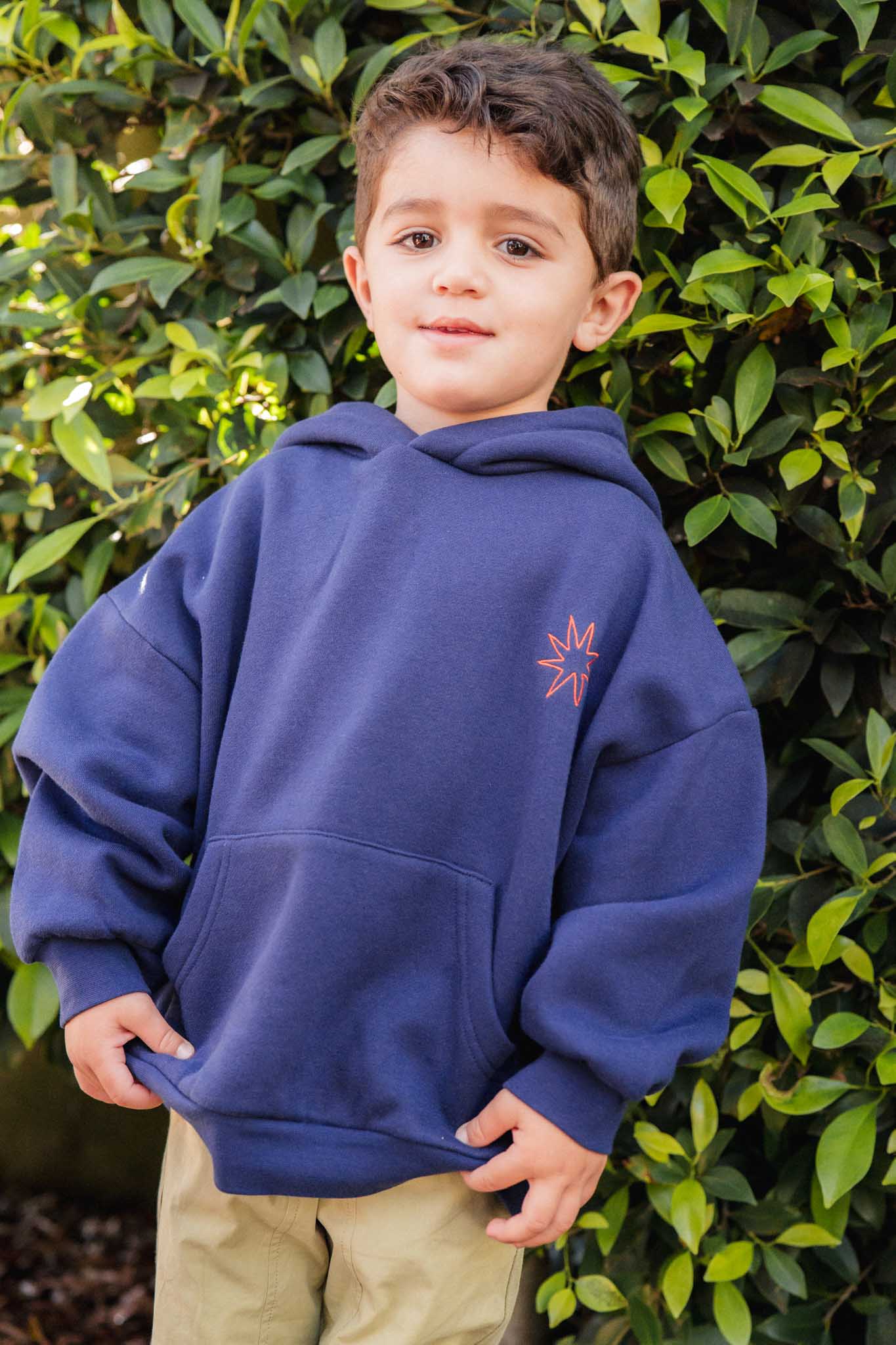 Child wearing a blue hoodie with a logo in front of green foliage