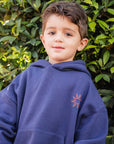 Child wearing a blue hoodie with a logo in front of green foliage