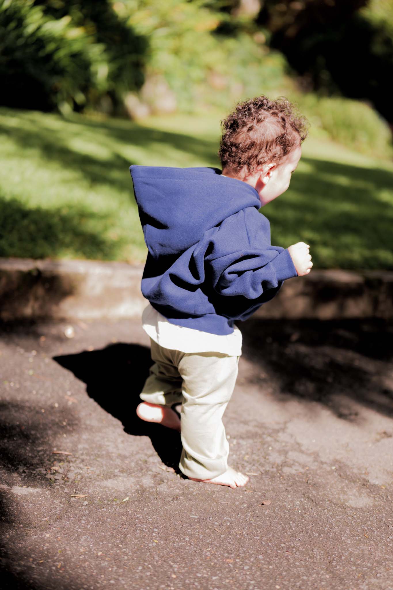 Child in a blue hoodie walking on a path with greenery in the background