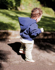 Child in a blue hoodie walking on a path with greenery in the background