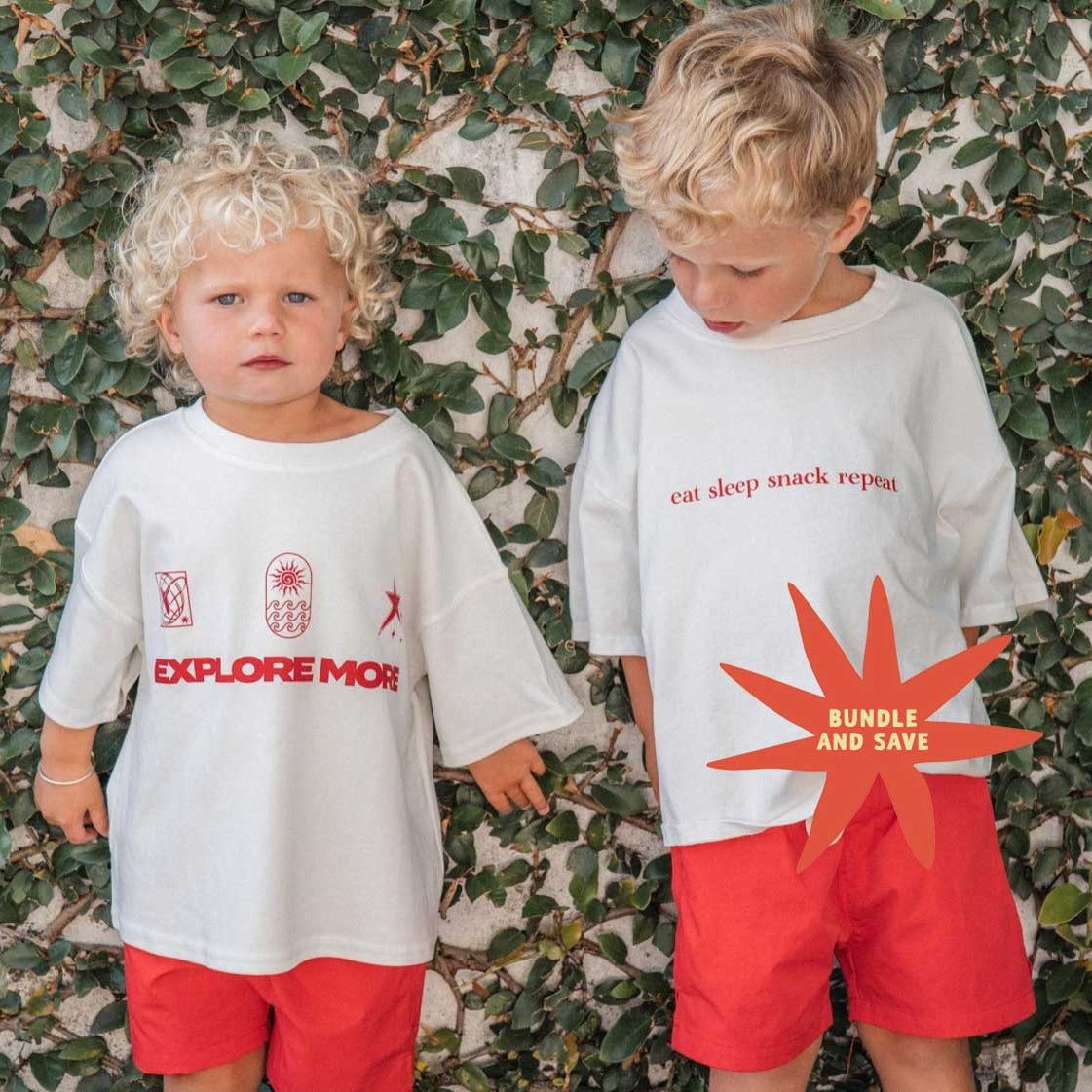Two children wearing white t-shirts with text and graphics against a leafy background
