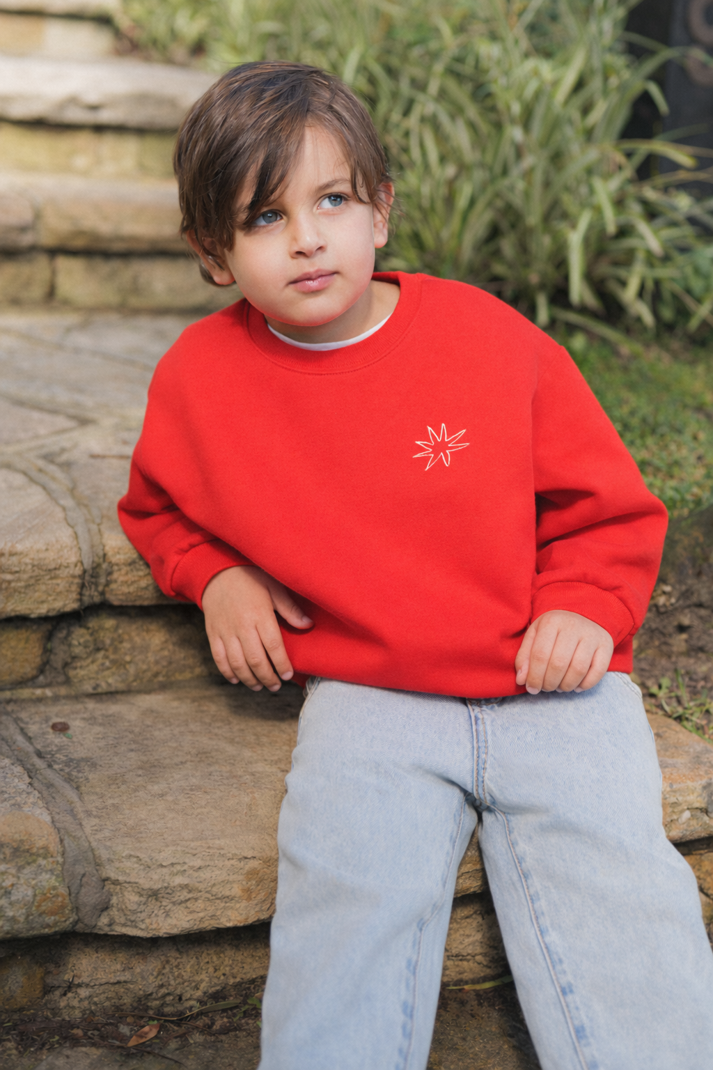 Child wearing a red sweatshirt with a logo, sitting on stone steps outdoors.