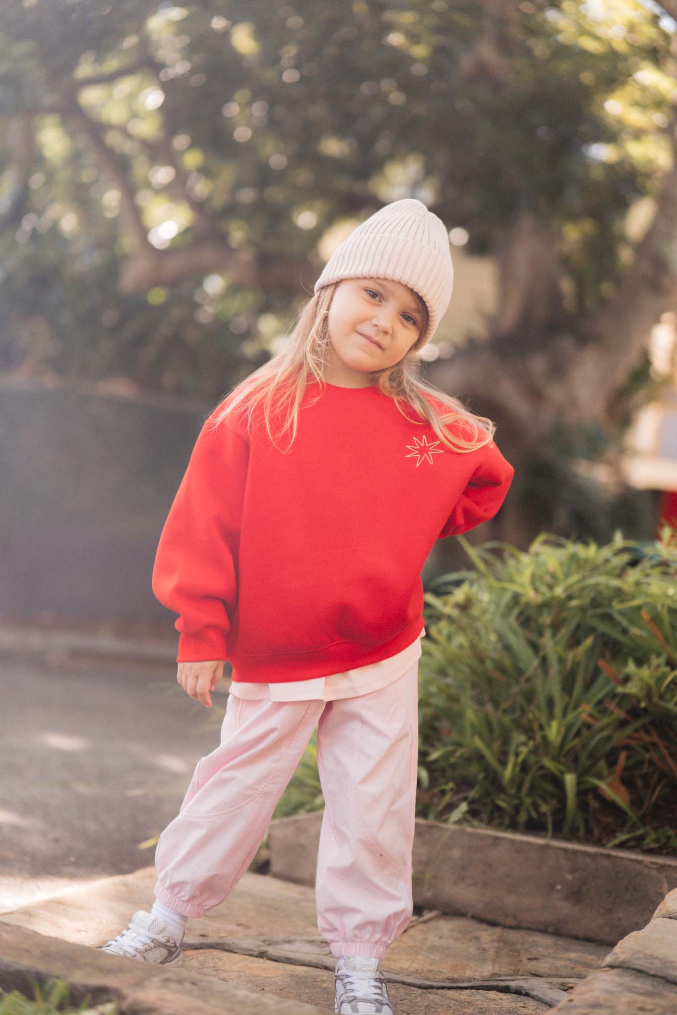 Child wearing a red sweater and pink pants standing outdoors with trees in the background
