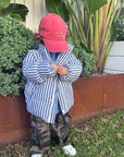 Child wearing a red cap and striped shirt standing in front of plants