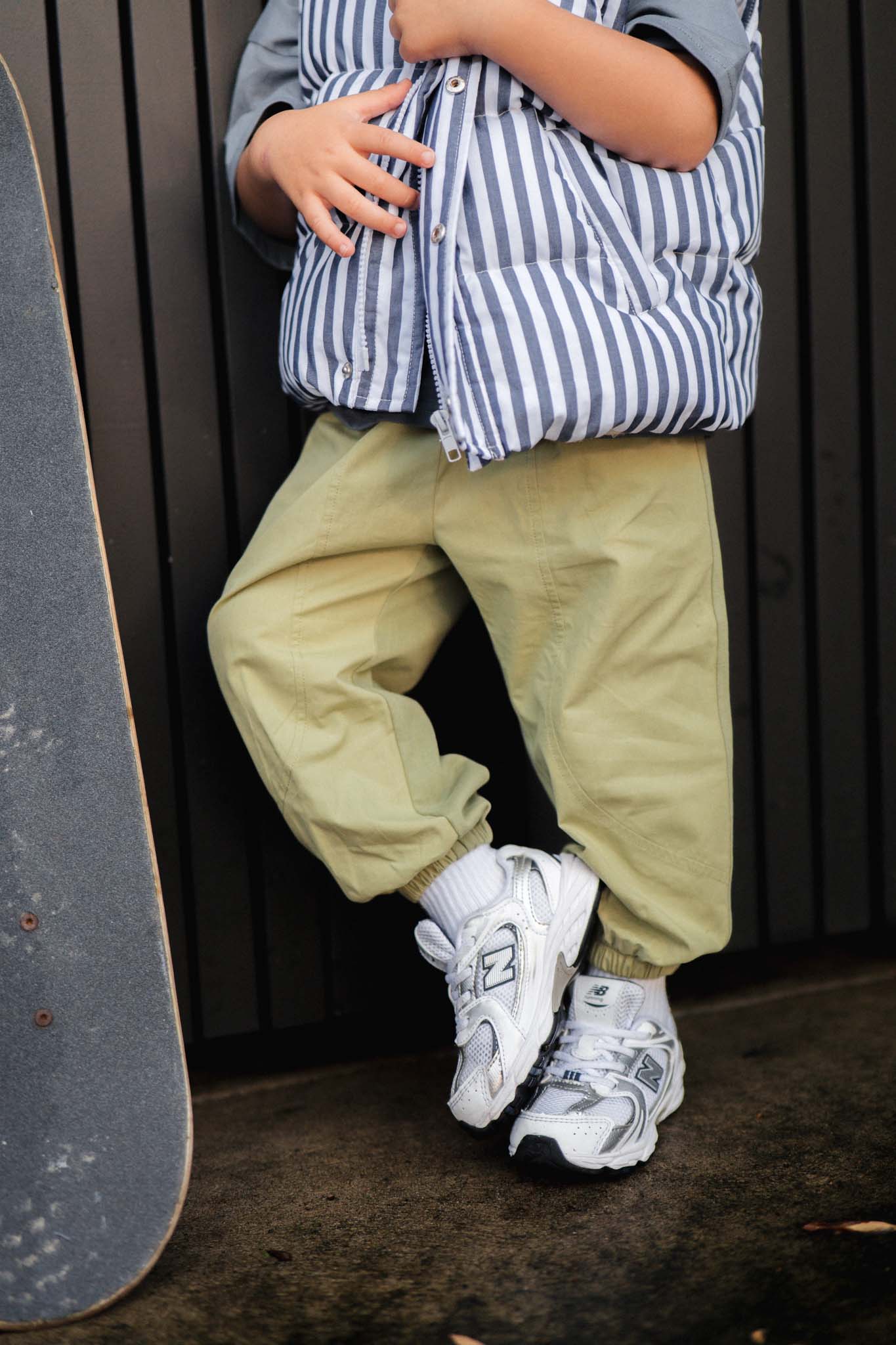 Person wearing a striped puffer and light green pants, and white sneakers with a skateboard.