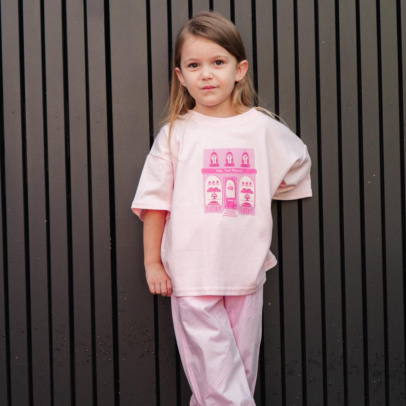 Child wearing a pink outfit with a graphic design against a dark vertical panel background
